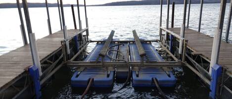 A pier with a wooden deck and metal railings, extending over calm water with a distant shoreline.