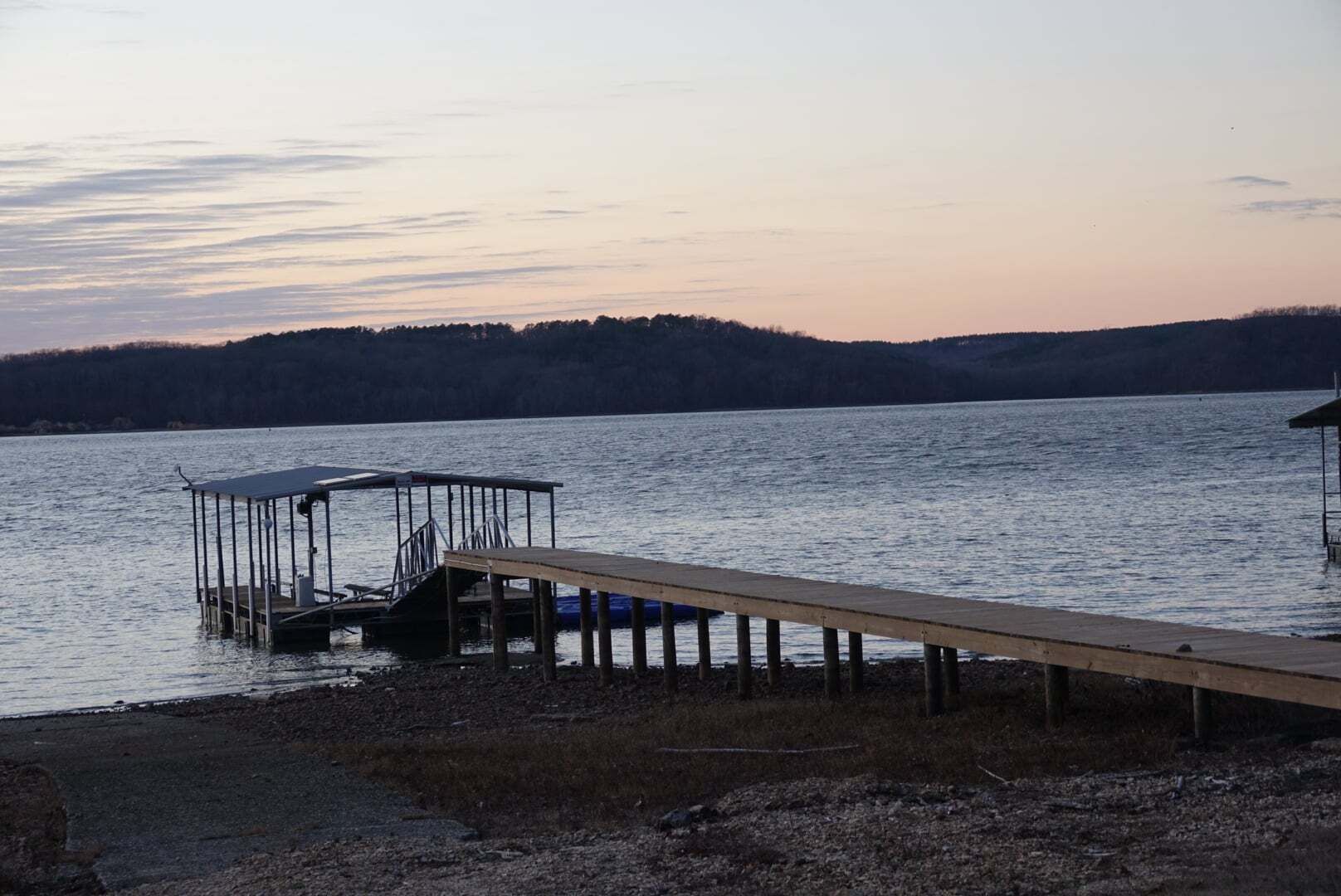 A dock extending into a calm lake with a forested hill in the background.