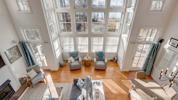 A spacious living room with a large window, a fireplace, and a dining area. - Eagle Roost Chalet- Modern Kentucky Lake Chalet (Waverly)