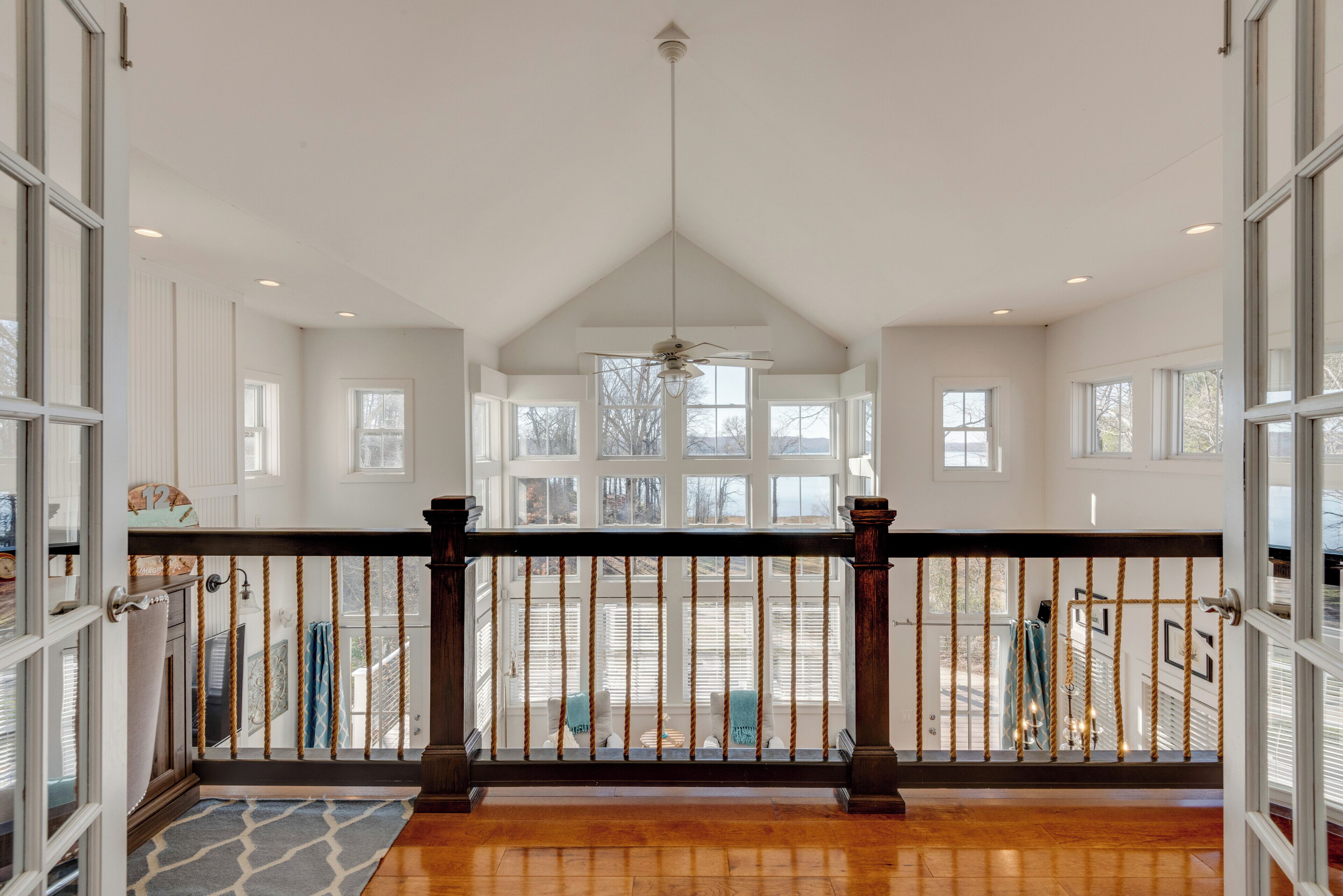 A spacious balcony with a wooden floor, a ceiling fan, and a view of a parking area.