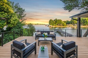 Una terraza con asientos al aire libre, una mesa con bebidas y vistas a un lago al atardecer.