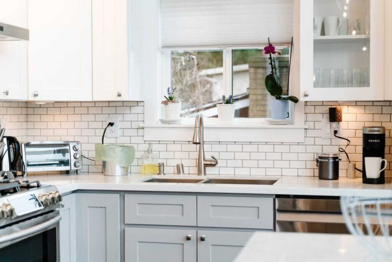 Una cocina moderna con armarios blancos, horno empotrado, lavamanos y cafetera.