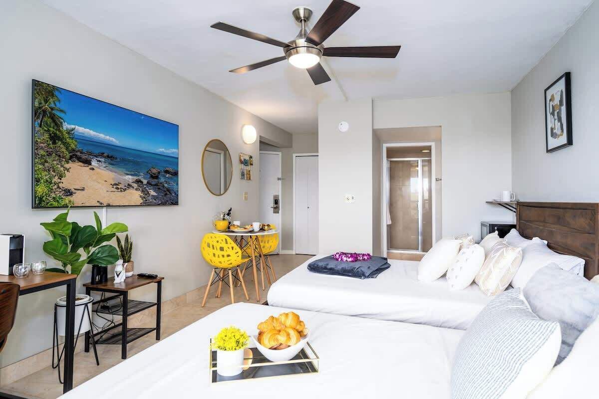A hotel room with a bed, a desk, a chair, a dining table, and a ceiling fan.