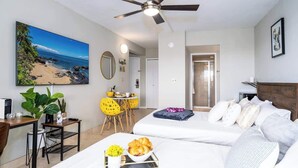 Quarto de hotel com cama, escrivaninha, cadeira, mesa de jantar e ventoinha no teto.