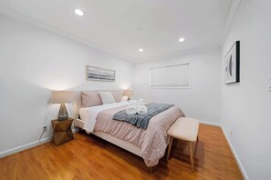 Ein Schlafzimmer mit einem Bett, Nachttischlampen, einer Bank und einem Fenster mit Jalousien.