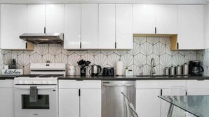A modern kitchen with white cabinets, a stainless steel dishwasher, and a built-in oven. - Marbella Lane - Your Cozy Haven 2BR Retreat (West Covina)