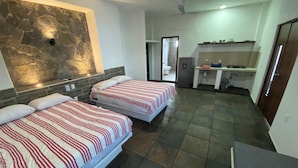 A hotel room with two beds, a stone accent wall, a kitchenette, and a bathroom visible through an open door. - Costa Ayala suite 8 with 2 dbl bed and 1 sofa, all basics, 2 blocks from beach (Los Ayala)