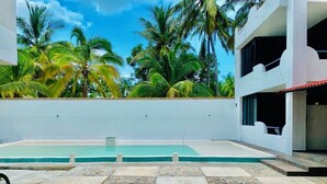 A swimming pool with a tiled deck, surrounded by palm trees and a clear sky. - Costa Ayala suite 8 with 2 dbl bed and 1 sofa, all basics, 2 blocks from beach (Los Ayala)