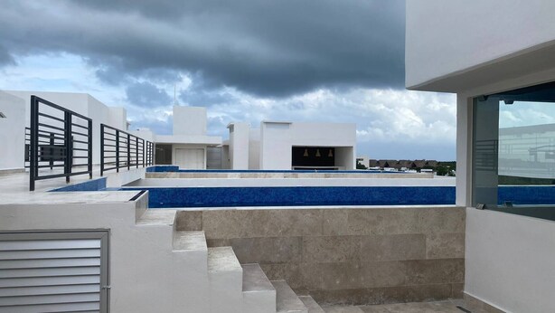 Eine moderne Dachterrasse mit Pool, Treppe zu einem überdachten Bereich und Blick auf die umliegende Landschaft.
