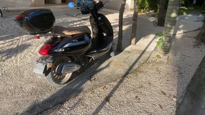 Ein schwarzer Roller steht auf einer Schotterauffahrt, im Hintergrund sind Palmen zu sehen.