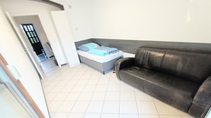 Una habitación con un sofá gris, una cama con ropa de cama azul y un suelo de baldosas.