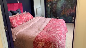 Une chambre à coucher avec un lit, une tête de lit rouge, une fresque murale et une porte.