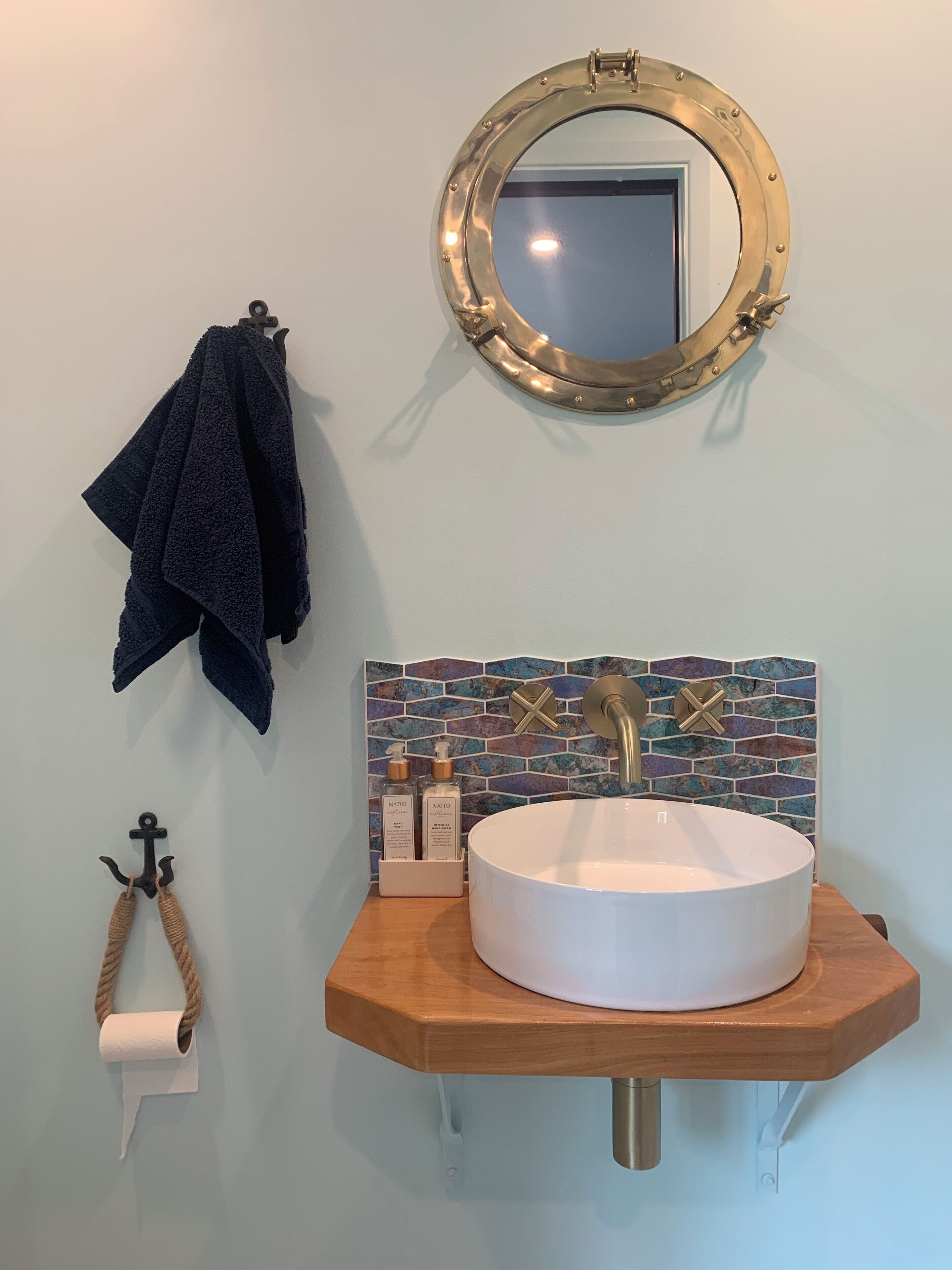 A bathroom with a round mirror, a wooden sink, and a tiled backsplash.