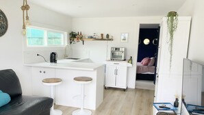 Un espace de vie compact comprenant un coin cuisine, un coin repas avec des tabourets, un canapé et un petit téléviseur.
