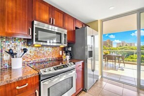Eine moderne Küche mit Edelstahlbackofen, Mikrowelle und Kühlschrank, einer gefliesten Spritzschutzwand und einem Balkon mit Tisch und Stühlen.