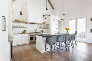 Une cuisine moderne avec des meubles blancs, un îlot central doté de tabourets et un éclairage suspendu.