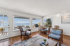 Ein geräumiges Zimmer mit großen Fenstern und Blick auf den Ozean, Holzboden sowie Möbel aus Holz und Polsterwaren.