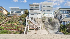 Una zona residencial costera con casas modernas, una escalera que conduce a un acantilado y una playa de arena.