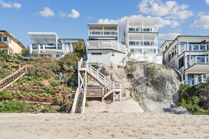 Ein Küstenwohngebiet mit modernen Häusern, einer Treppe, die zu einer Klippe führt, und einem Sandstrand.