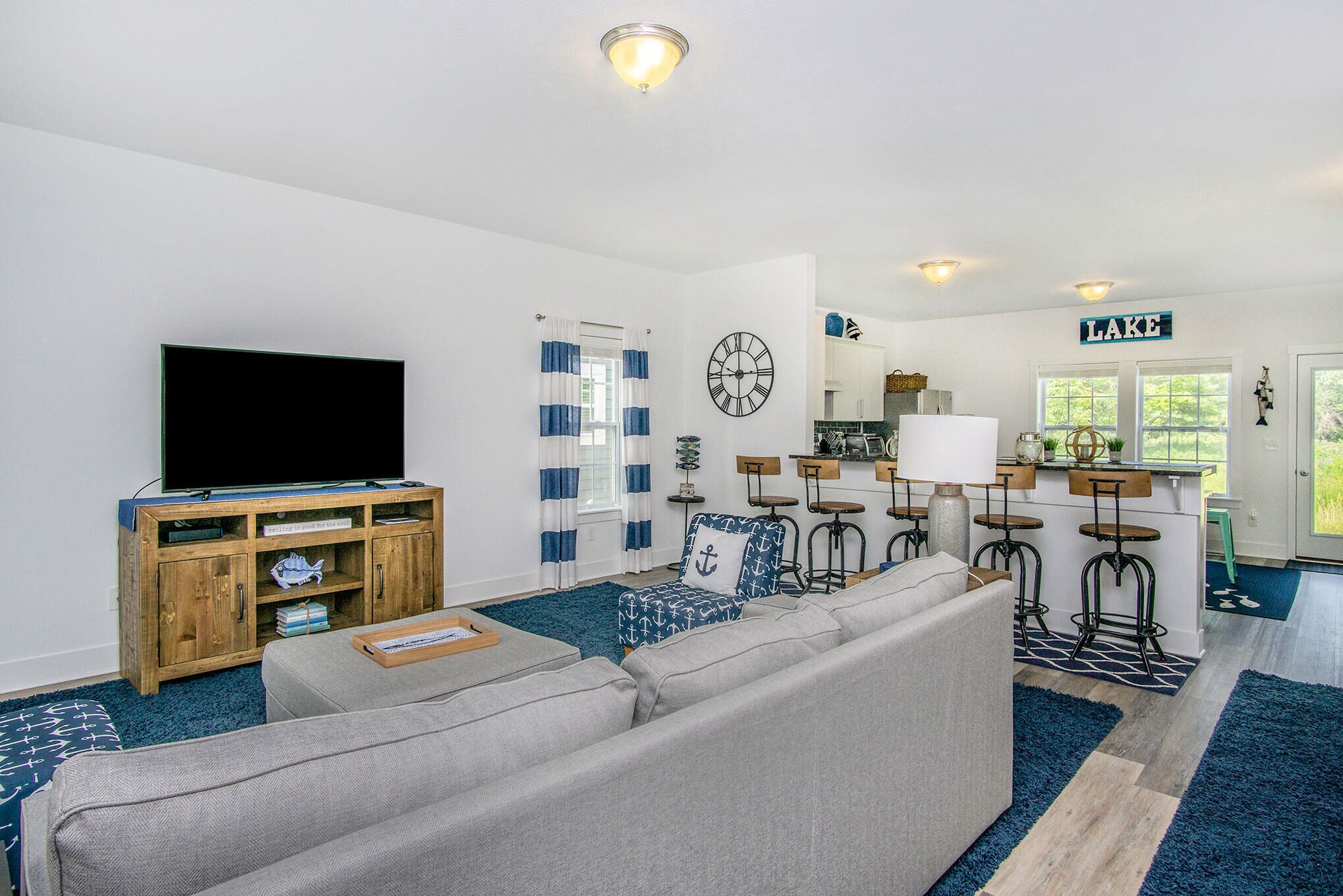 Ein modernes Wohnzimmer mit Flachbildfernseher, grauem Sofa, Holzschrank und Küchenzeile mit Barhocker.