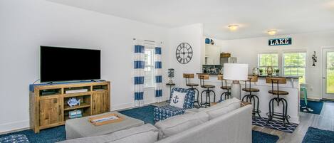 Ein modernes Wohnzimmer mit Flachbildfernseher, grauem Sofa, Holzschrank und Küchenzeile mit Barhocker.