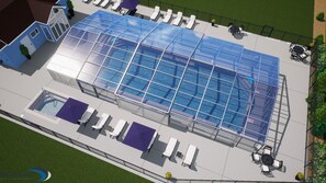 A swimming pool with a glass enclosure, surrounded by lounge chairs and tables, and adjacent to a building with a blue facade. - Relax and play at Indigo Haven--spacious home close to beach and pools! (South Haven)