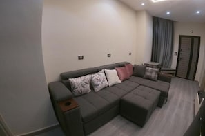 Un saló modern amb un sofà modular, una taula auxiliar petita i una porta al fons.