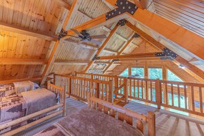A high-ceilinged wooden cabin with a sloped roof, a bed with a headboard, and a window overlooking a natural landscape. - Bear Bluff Cabin / HOT TUB / EV Charge / Sleeps 10 / 3k sq ft / 10 acres (De Soto)