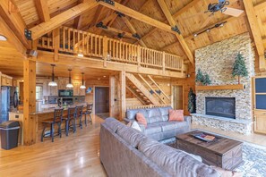 A spacious living area with a high ceiling, a stone fireplace, and a wooden staircase. - Bear Bluff Cabin / HOT TUB / EV Charge / Sleeps 10 / 3k sq ft / 10 acres (De Soto)