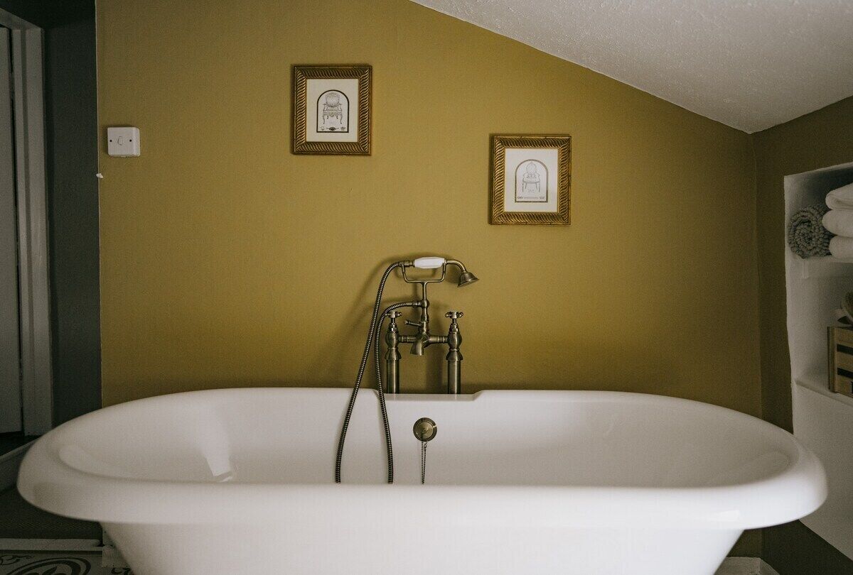 A bathroom with a freestanding bathtub, two framed pictures on the wall, and a towel rack with towels.