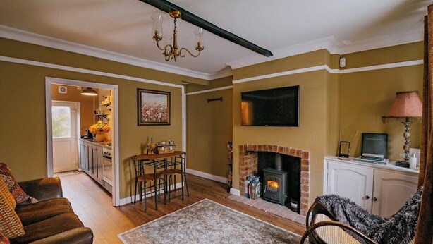 A living room with a fireplace, a dining area, and a kitchen visible through an open door. - Rasen Stay Cottage - Cosy Vintage  Retreat in Lincoln (Lincoln)