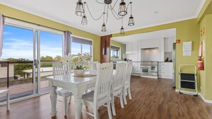 A spacious kitchen with white cabinets, a stainless steel oven, and a dining area with a white table and chairs. - Big Red Beach House - Rainbow Beach (Rainbow Beach)