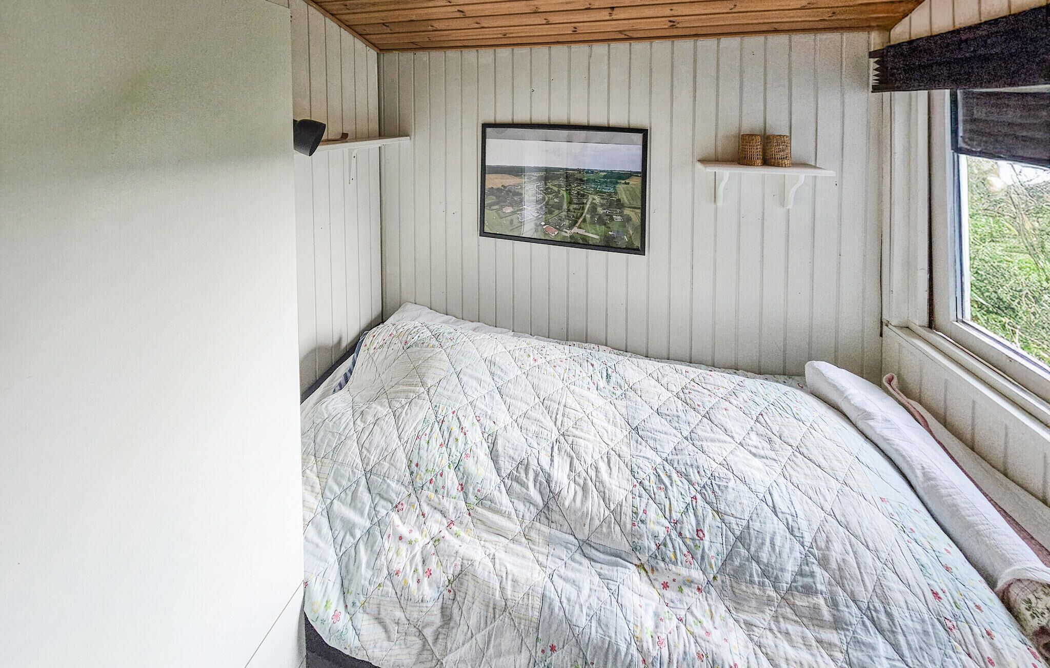 A bedroom with a bed, a framed picture on the wall, and a window with a view of greenery.