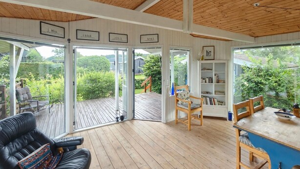 Un vaste espace de vie avec une terrasse en bois, un canapé en cuir noir et une table à manger en bois.