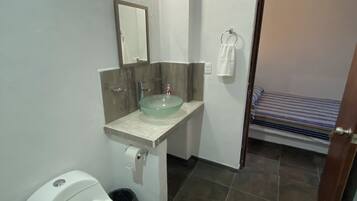 A bathroom with a toilet, a glass sink, a mirror, and a towel ring.