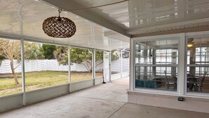 Ein überdachter Patio-Bereich mit großen Fenstern, einer hängenden Leuchte und Blick auf den Garten.