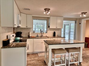 Une cuisine moderne avec des meubles blancs, des plans de travail en granit et un îlot central doté de tabourets.