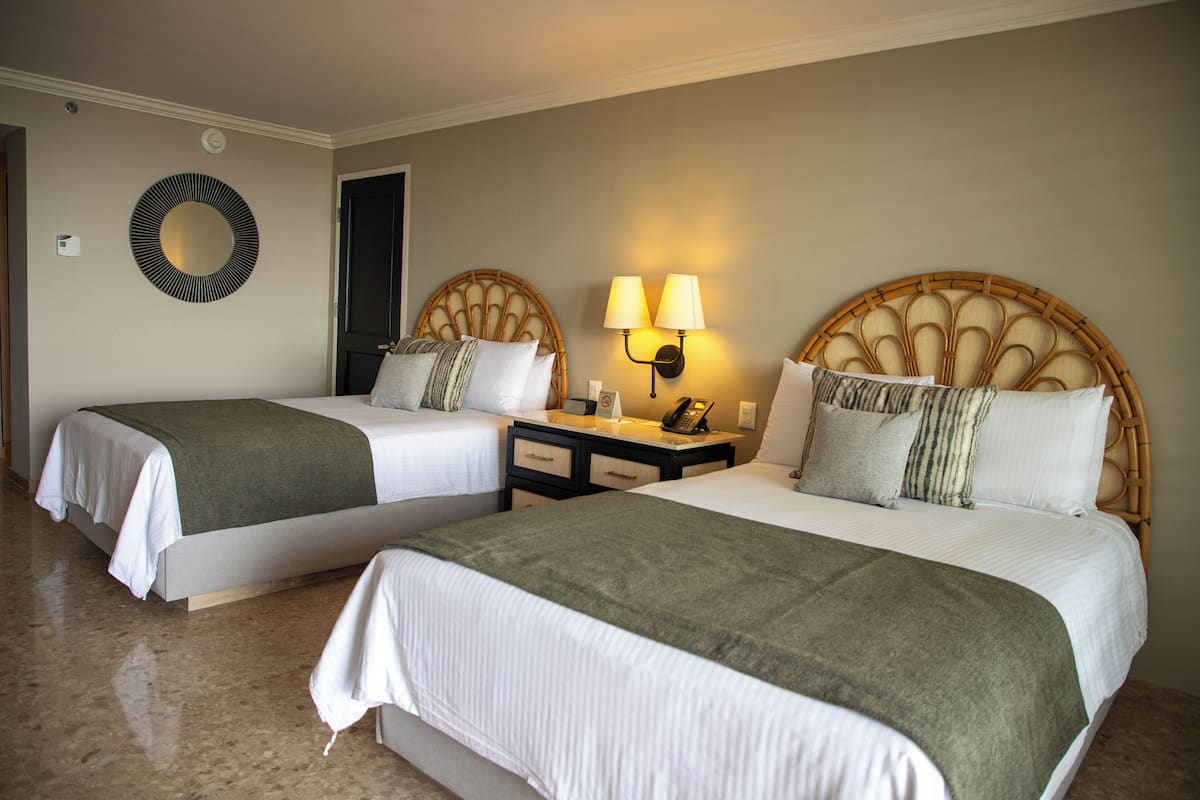Two twin beds with green throw blankets, a wall-mounted circular mirror, and a nightstand with a lamp.