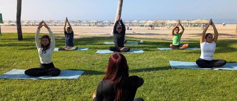 A group of people performing yoga on mats in a grassy area with a beach in the background.