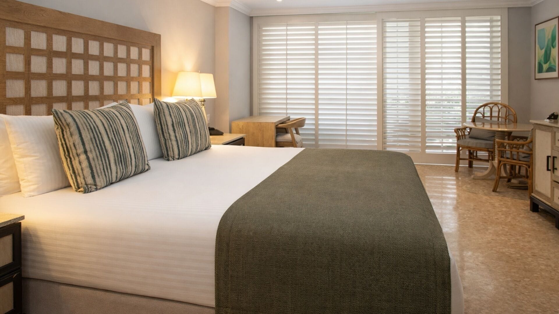 A hotel room with a large bed, a desk, a chair, and a window with blinds.