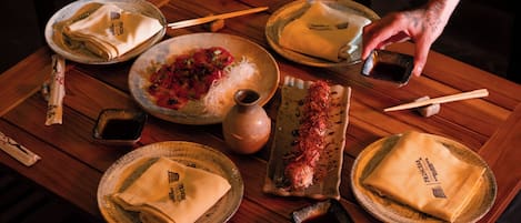 Mesa de madera con platos, palillos y una mano alcanzando un plato.