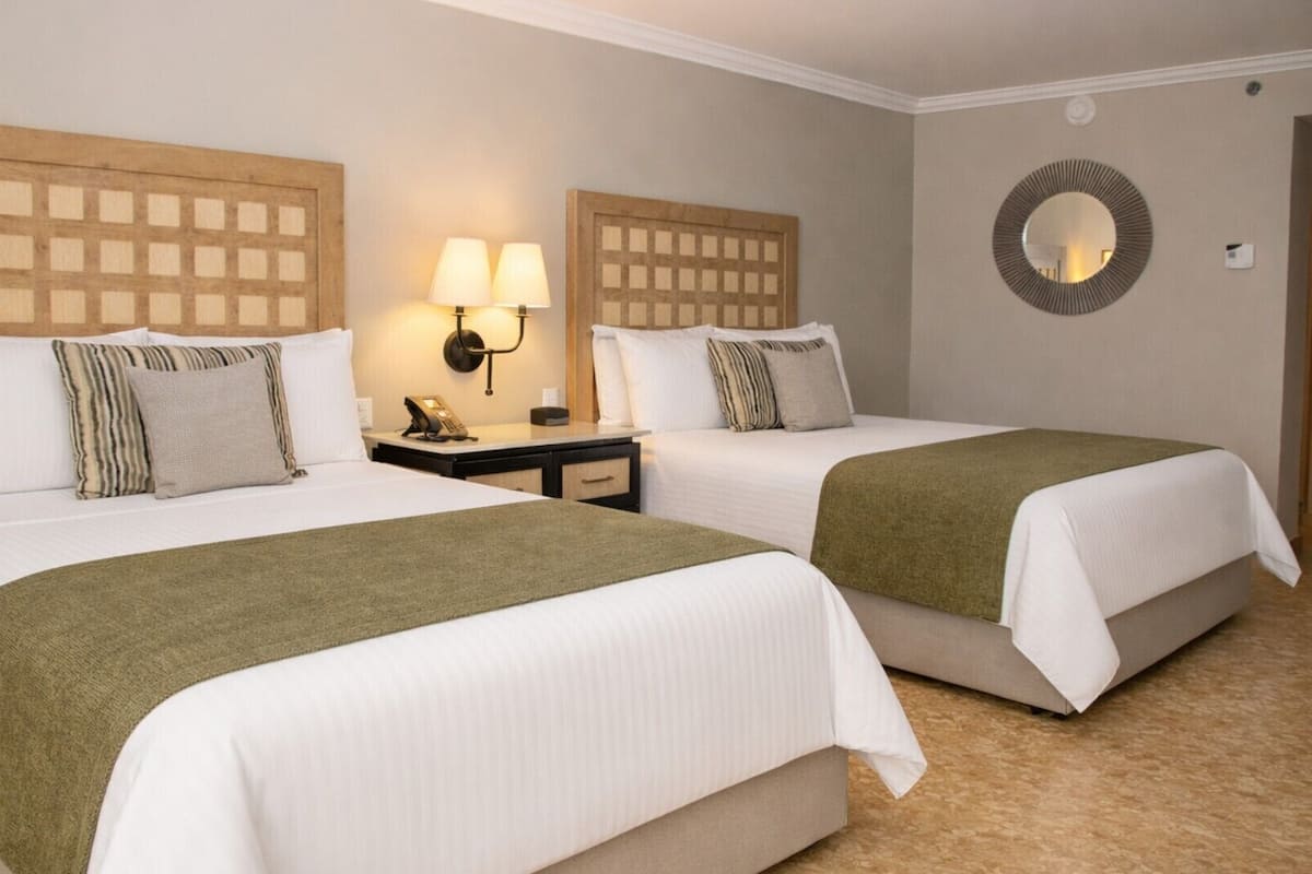 A hotel room with two beds, a nightstand with a lamp, and a mirror on the wall.