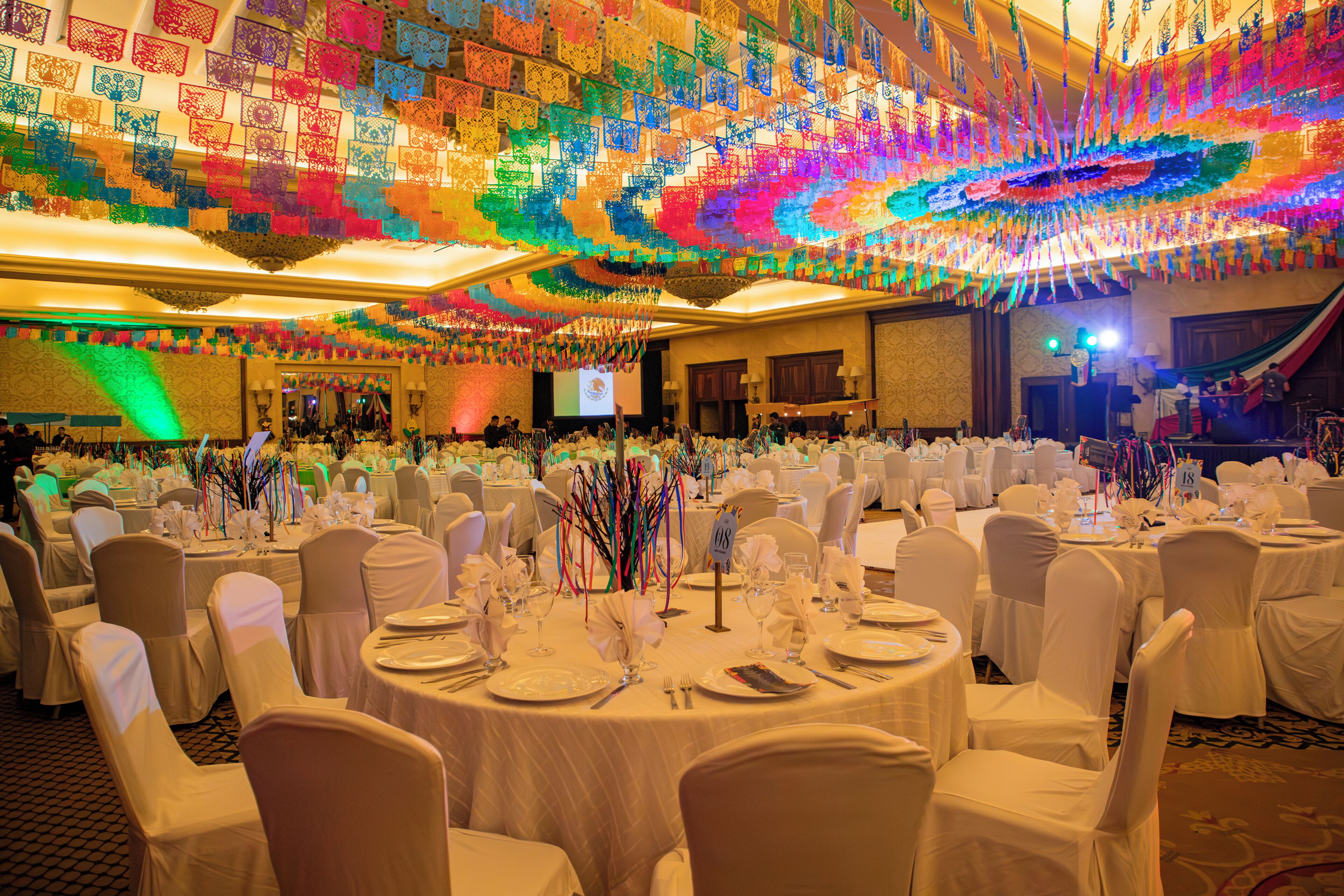 A banquet hall with round tables set for a formal event, decorated with white tablecloths and chairs covered in white fabric.