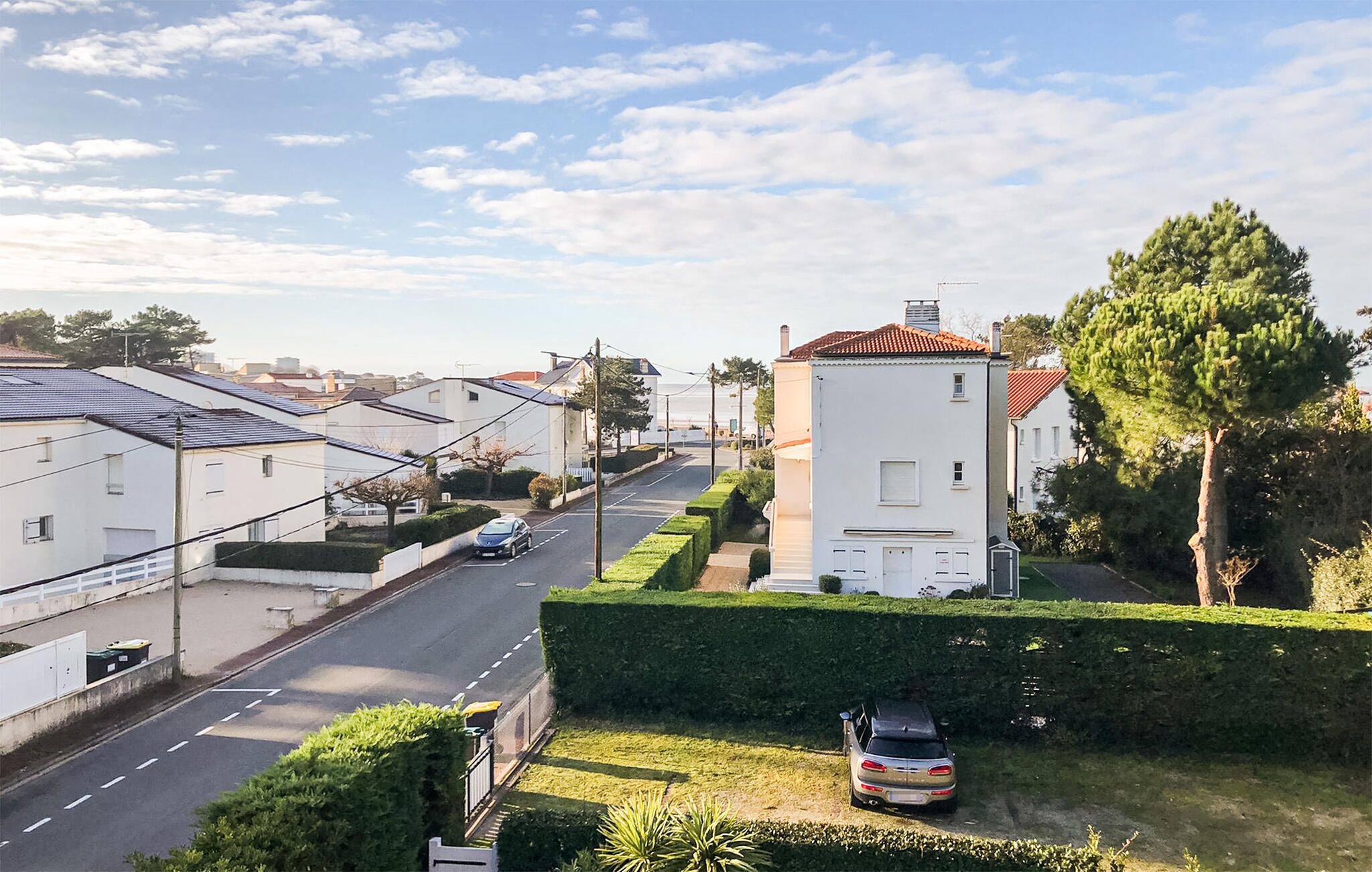 A residential street with houses, a car parked on the side, and a clear sky.