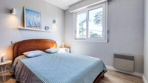 Un dormitorio con cama, ventana, un cuadro colgado en la pared y un calefactor.