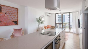 Une cuisine moderne dotée d’un îlot central, d’un four encastré et d’une grande fenêtre offrant une vue sur la ville.