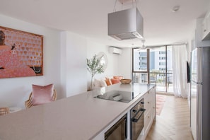 A modern kitchen with a central island, a built-in oven, and a large window offering a view of the city. - Blush by Khove (Burleigh Heads)
