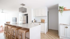 Une cuisine moderne avec des meubles blancs, un îlot central doté de tabourets, des appareils en acier inoxydable et un plancher en bois disposé en chevrons.
