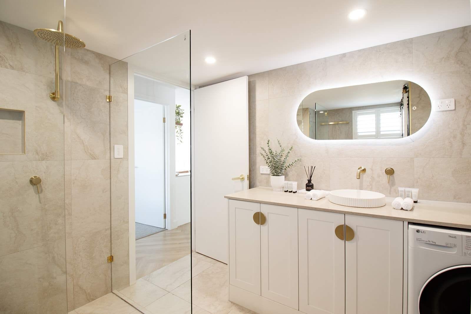A modern bathroom with a glass-enclosed shower, a round mirror, and a built-in washing machine.