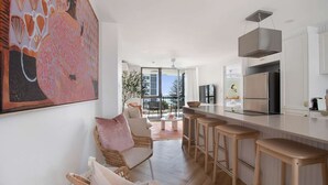 Une cuisine moderne avec un coin bar, un espace repas doté de meubles en osier et une grande fenêtre donnant sur un balcon.